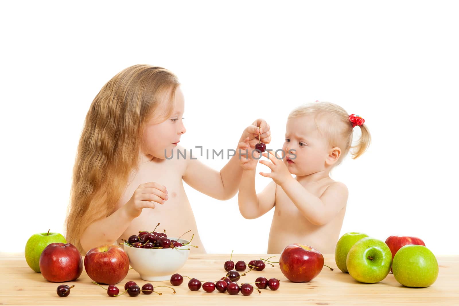 two little girls eat fruit at a table on the isolated background