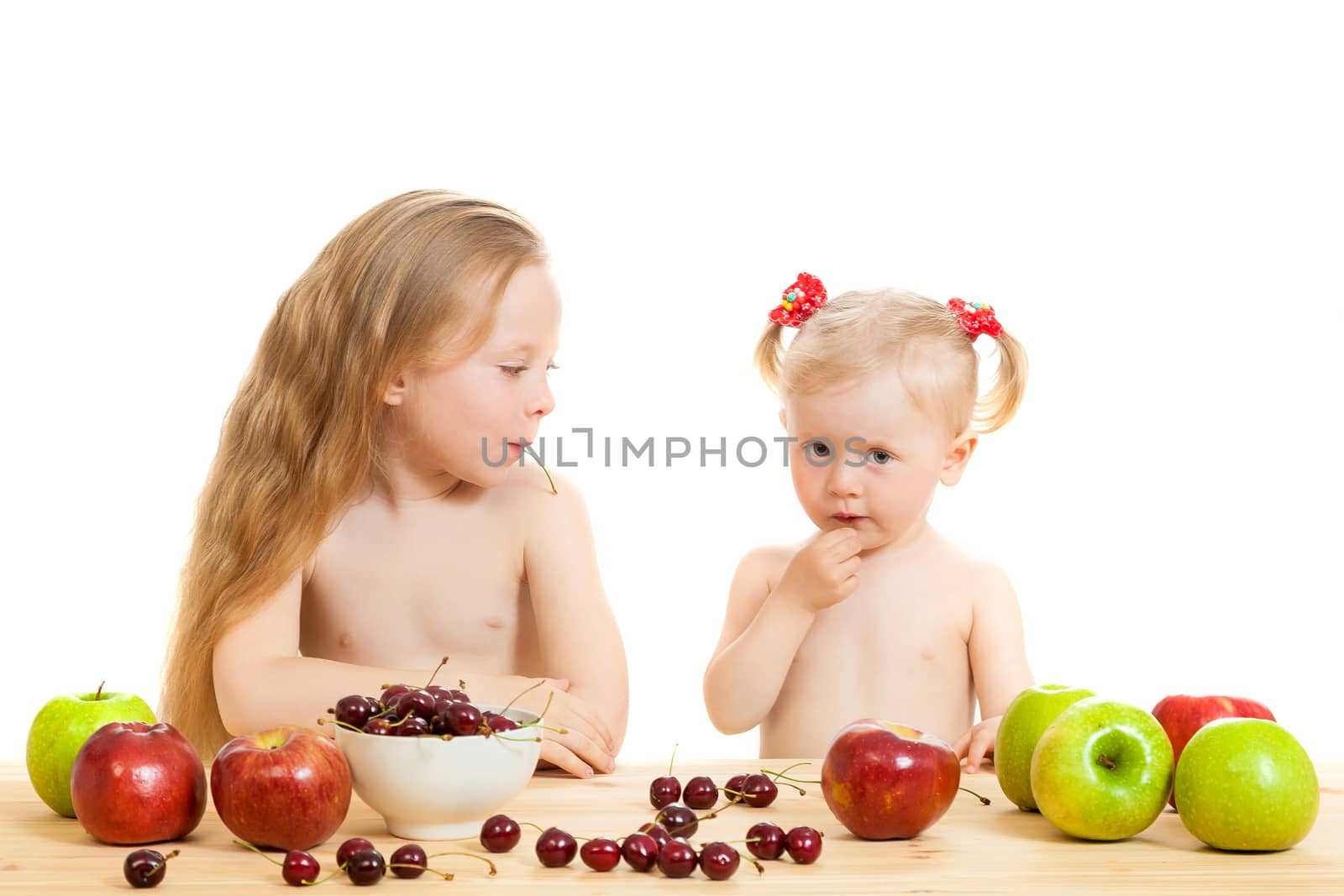 two little girls eat fruit at a table on the isolated background