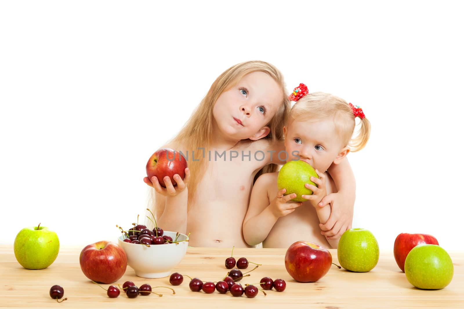 two little girls eat fruit at a table on the isolated background