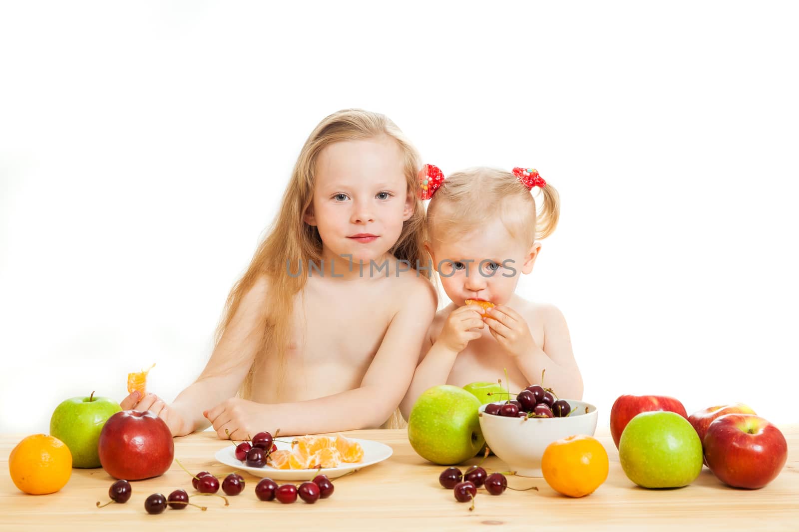 two little girls eat fruit at a table on the isolated background