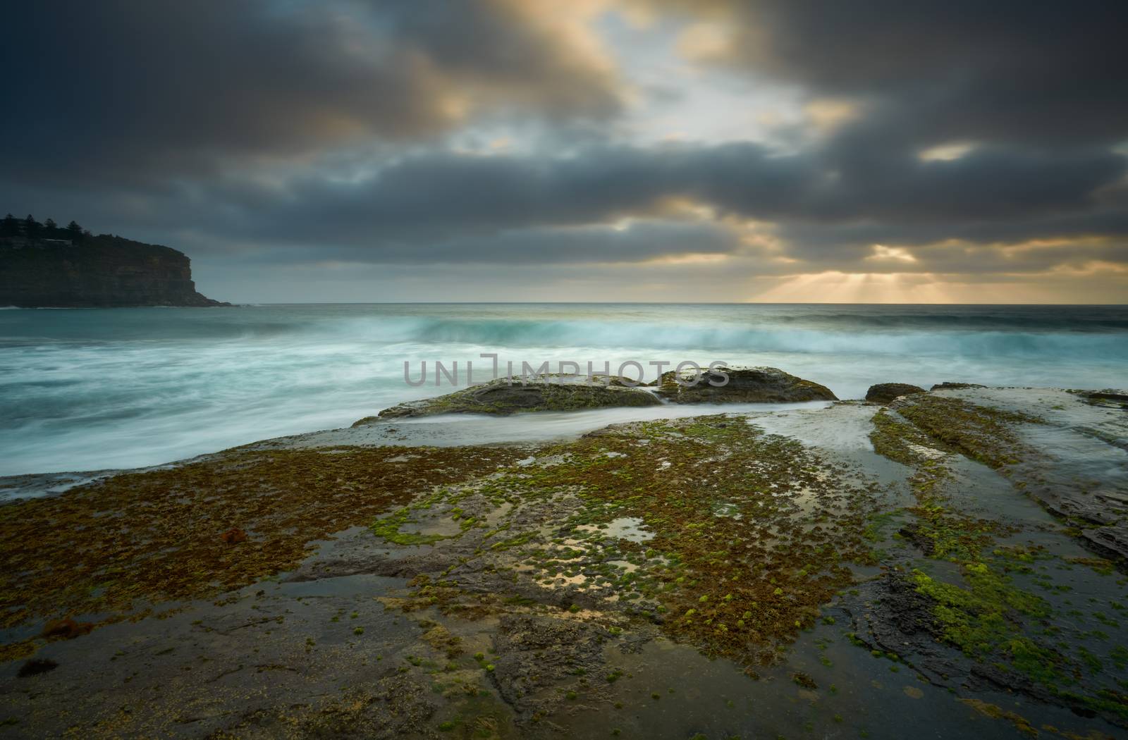 Moody clouds leave a small break for the sunrays to peak through on the low tidal rockshelf at Bilgola