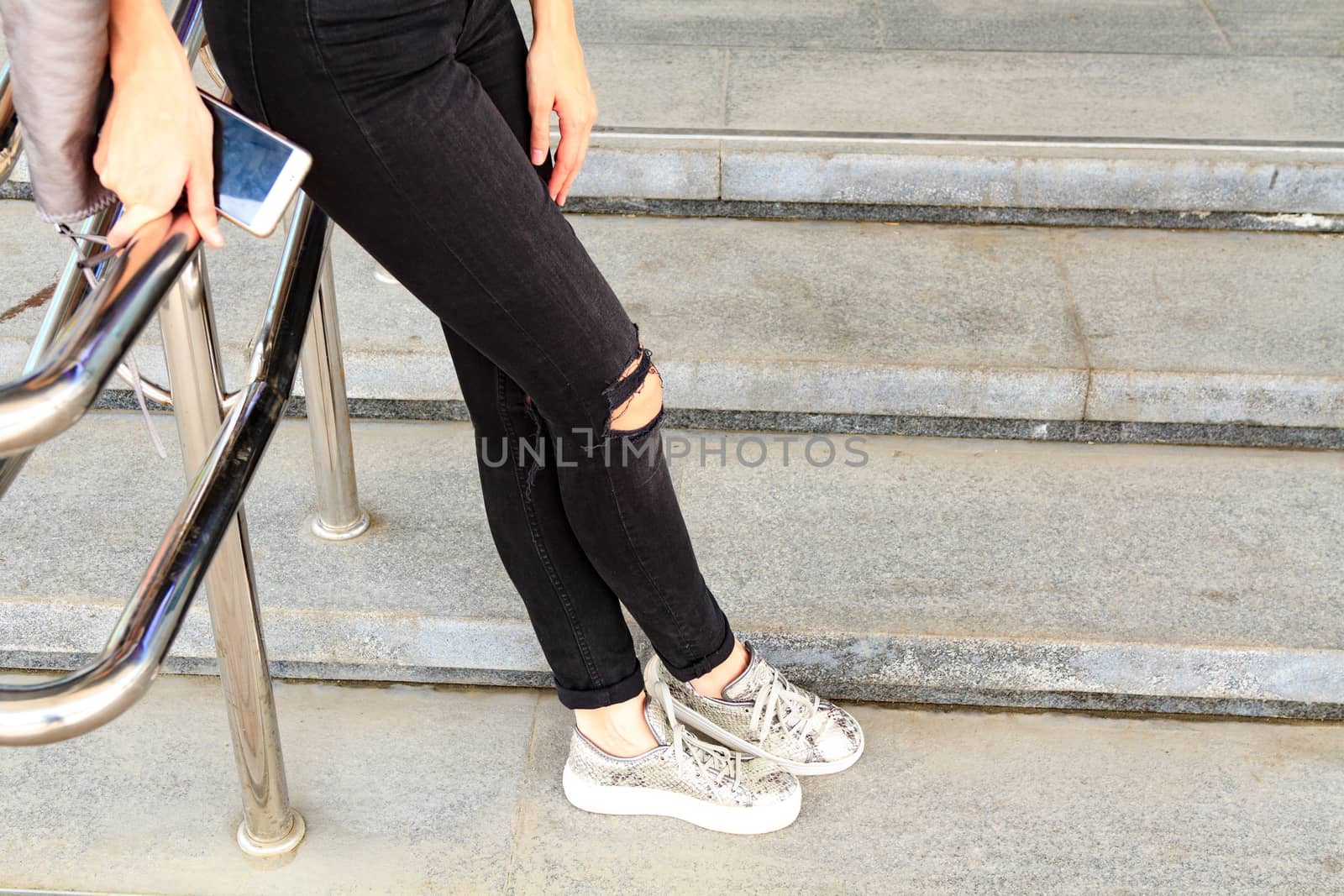 Woman's long legs in black jeans pants on a stone stairs