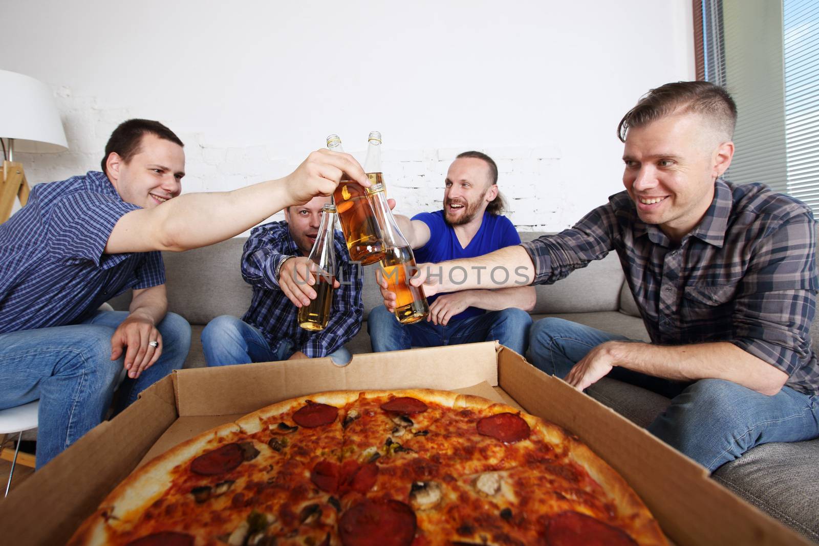 Male friends sitting at home on couch, clink beer, going to eat pizza, celebrating something