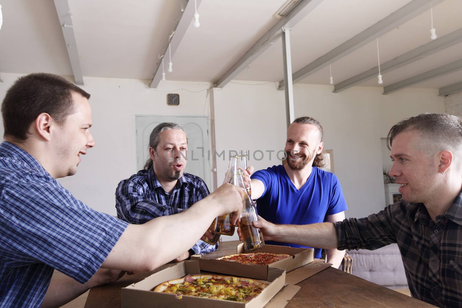 Friends clink beer over pizza by destillat