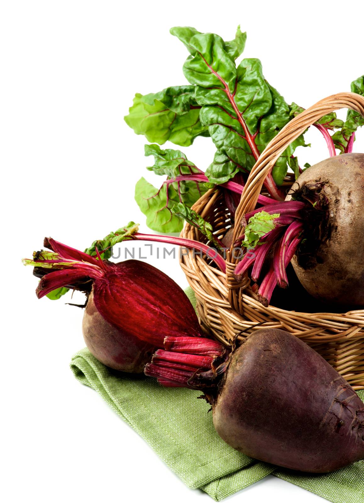 Arrangement Fresh Raw Organic Beet Roots with Green Beet Tops in Wicker Basket on Napkin isolated on White background