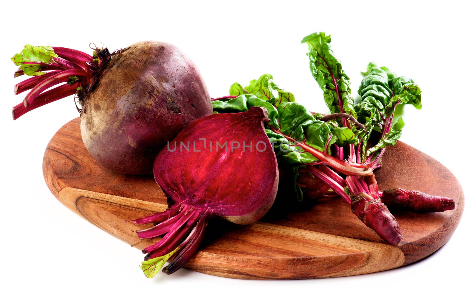 Arrangement of Full Body, Half and Young Sprouts of  Fresh Raw Organic Beet Roots with Green Beet Tops on Wooden Cutting Board isolated on White background