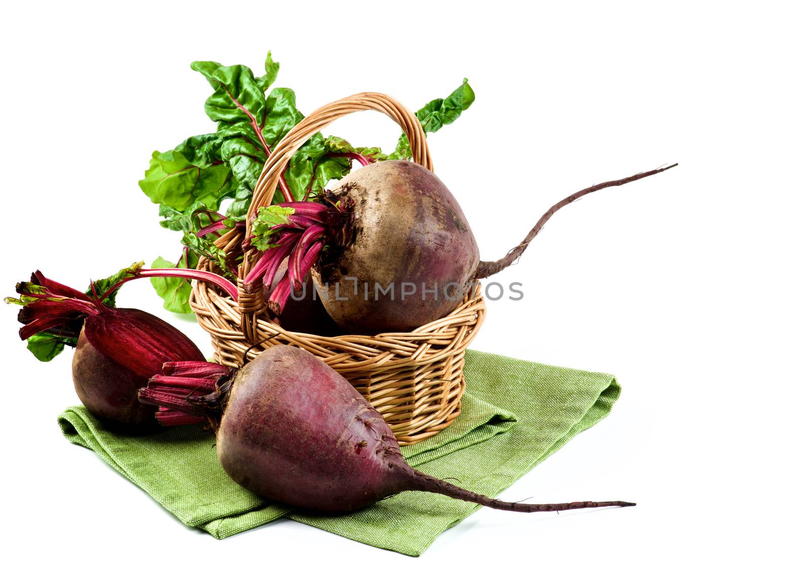 Arrangement of Full Body and Half of Fresh Raw Organic Beet Roots with Green Beet Tops in Wicker Basket on Napkin isolated on White background