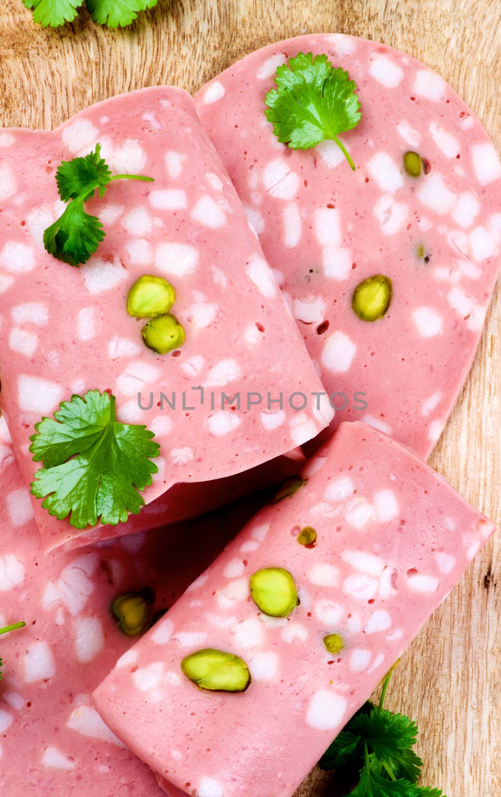Slices of Delicious Fresh Mortadella with Pistachio and Greens closeup on Wooden background