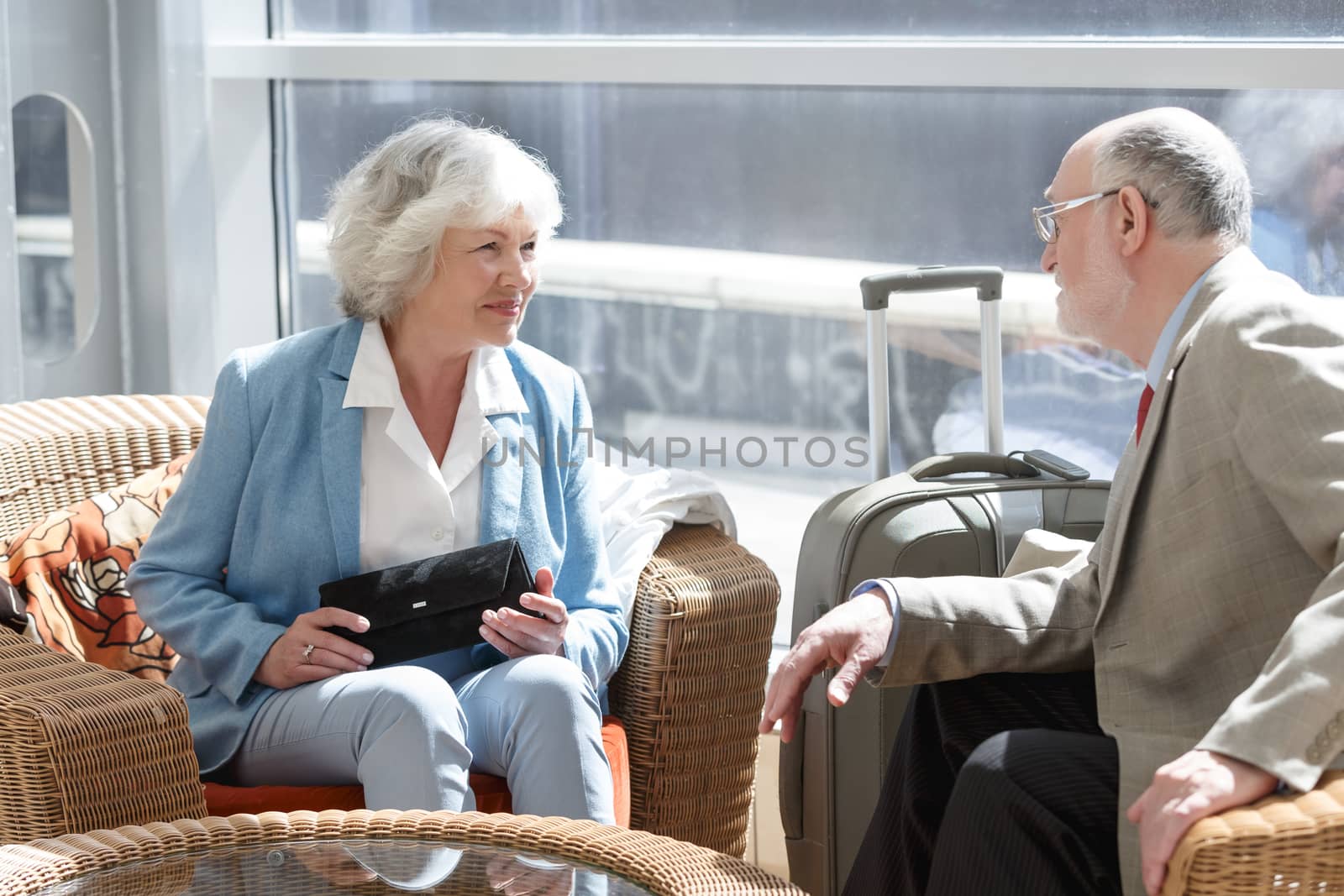 Senior couple of tourists waiting for their flight sitting with suitcase and talking