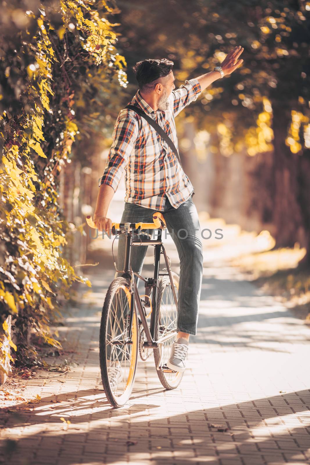 Casual businessman going to work by bicycle and waving Hello.