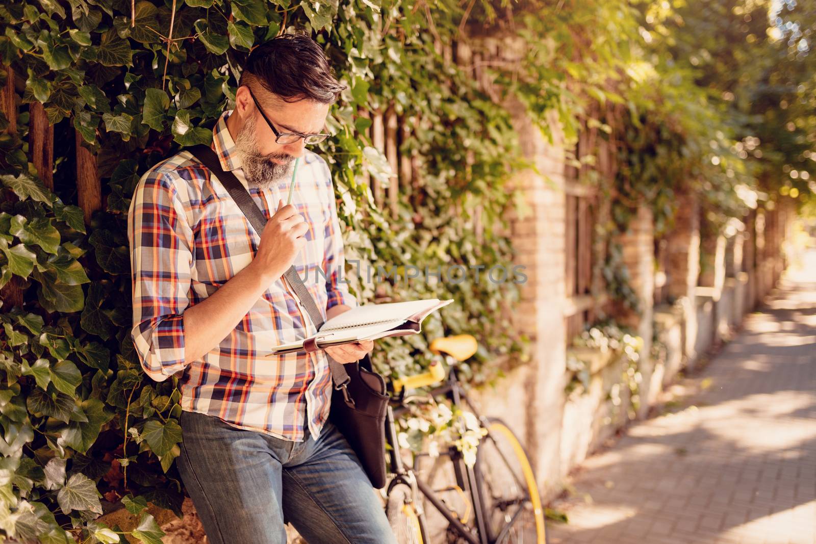 Pensive casual businessman working outdoor. He is standing against the wall next to bike.