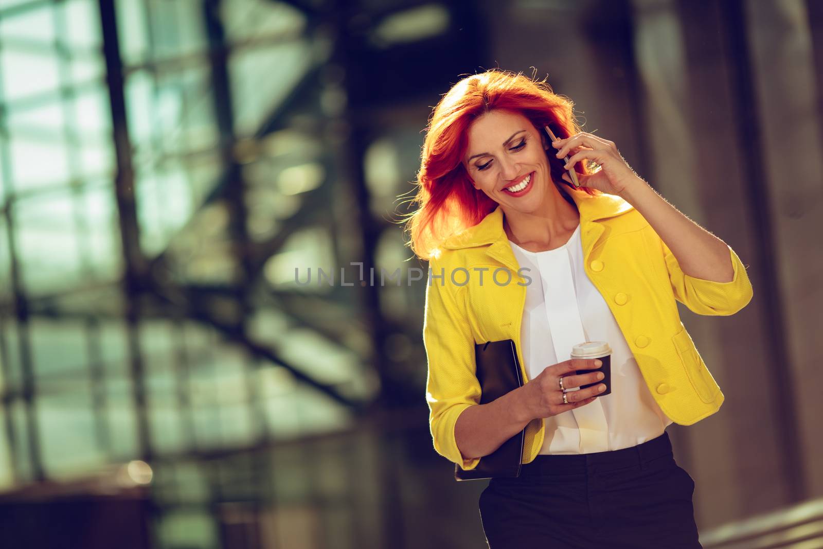 Smiling successful businesswoman using smartphone on coffee break in office district. 