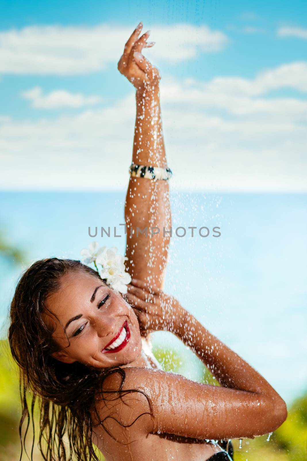Beautiful young woman enjoying under a shower on the beach. 