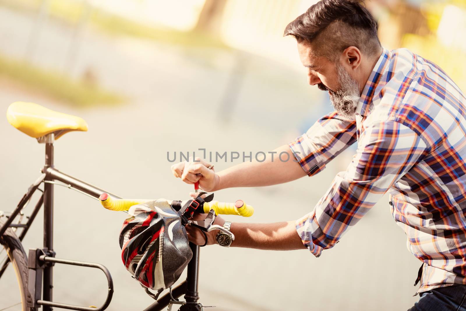 Casual businessman going to work by bicycle. He is repairing bicycle handlebar on a street.