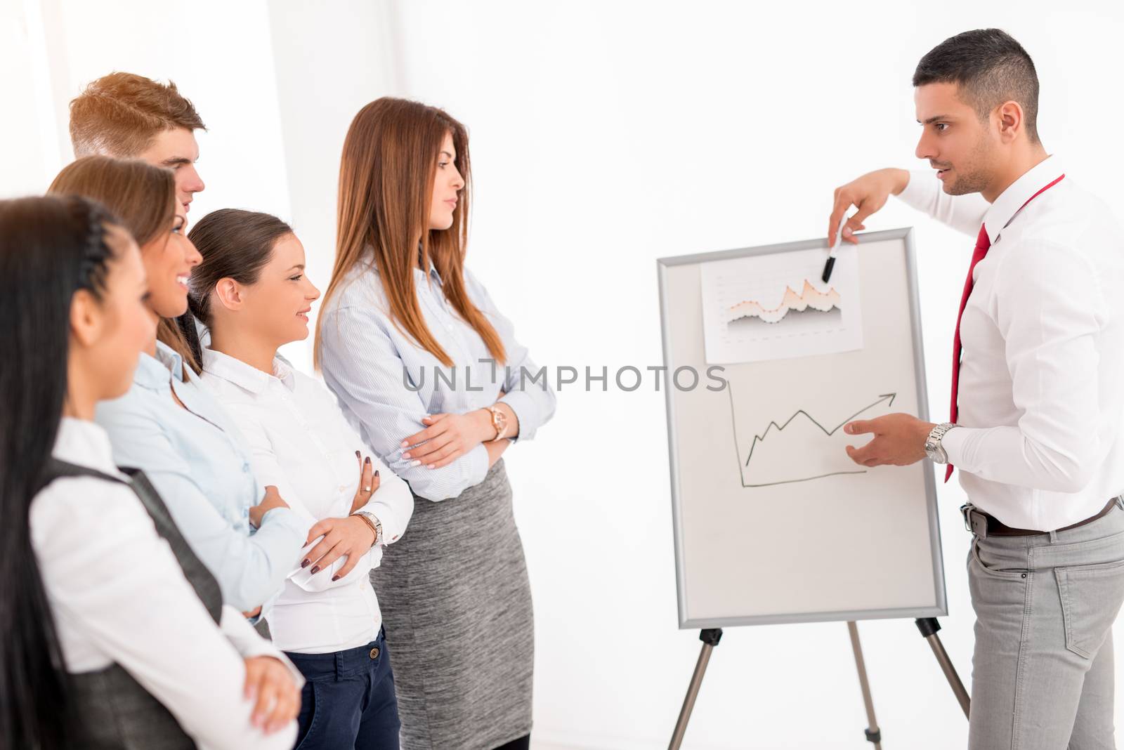 Businesspeople having meeting in a office. Young businessman standing  in front of flip chart and having presentation.