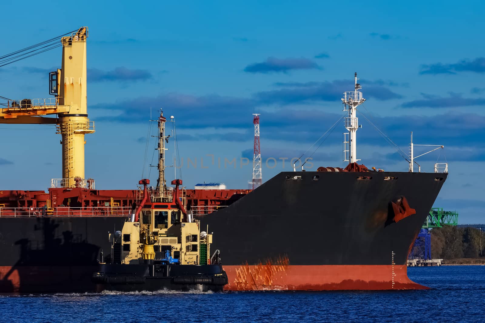 Black cargo ship mooring at the port with tug ship support