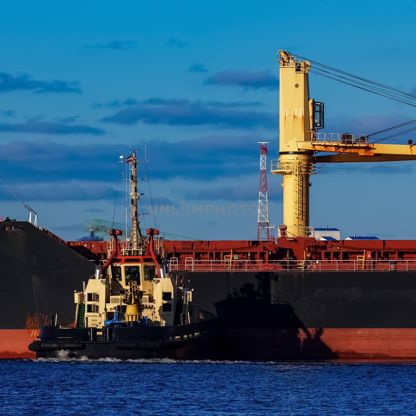 Black cargo ship mooring at the port with tug ship support