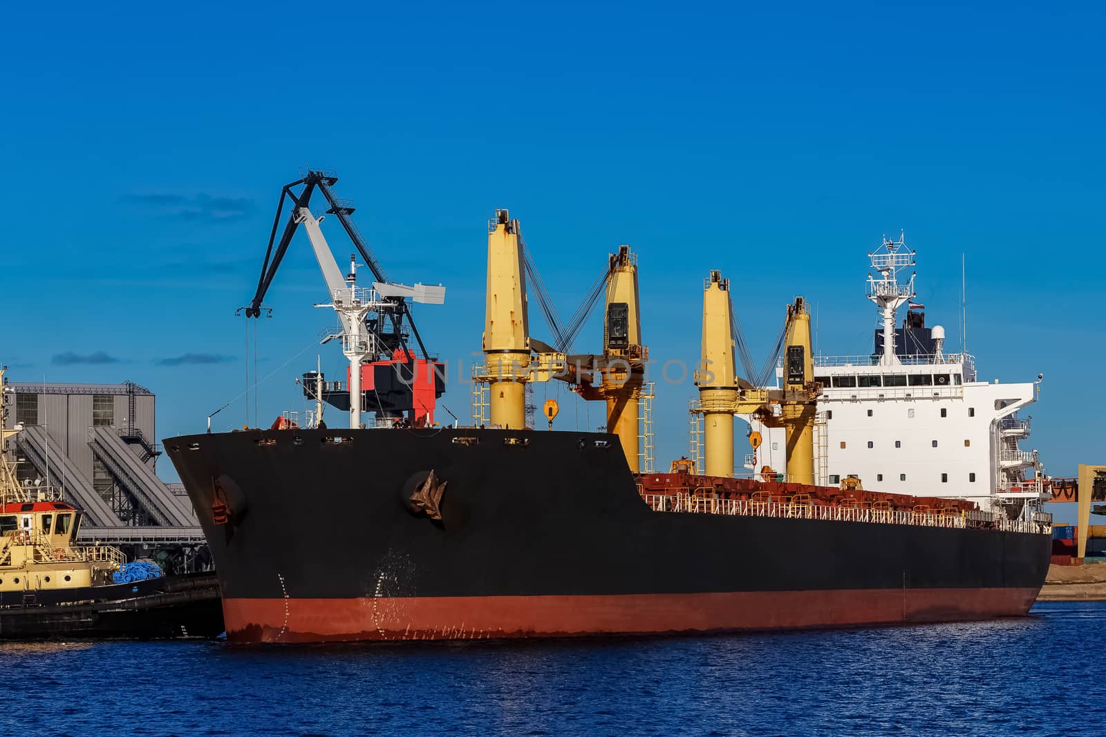 Black cargo ship mooring at the port with tug ship support