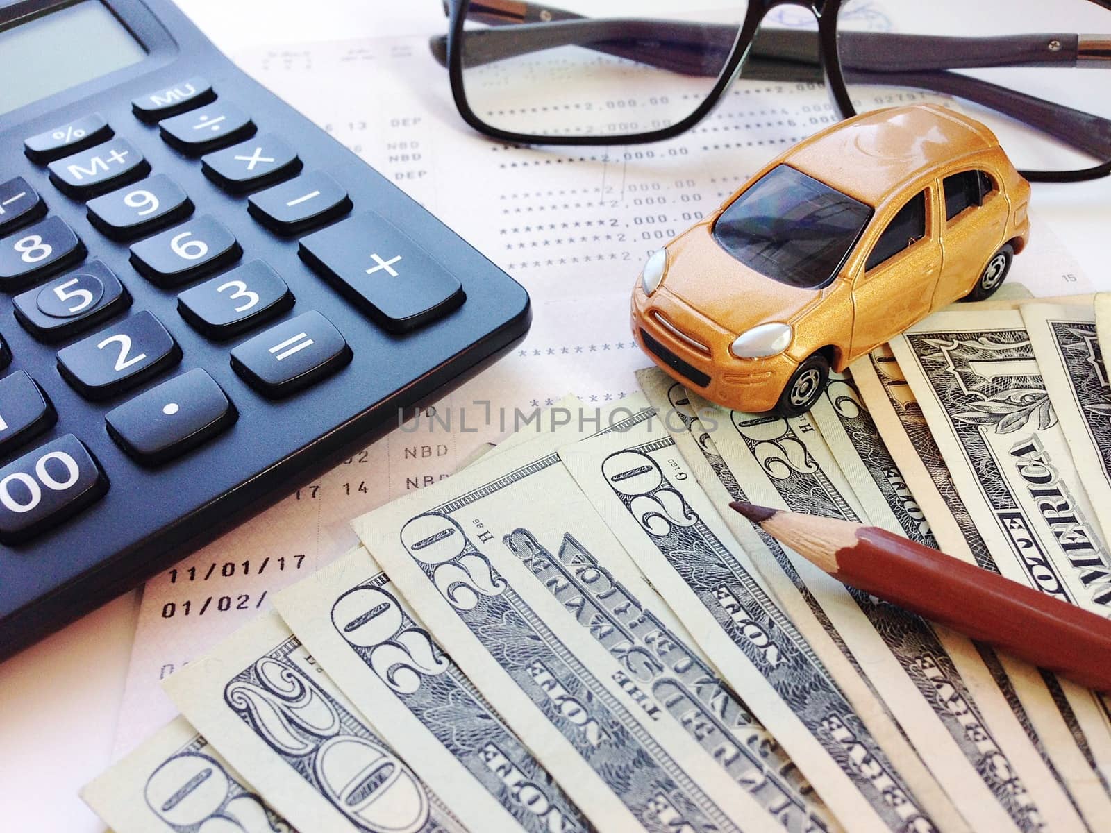 Business, finance, savings, banking or car loan concept : Miniature car model, pencil, money, calculator, eyeglasses and savings account passbook or financial statement on white background