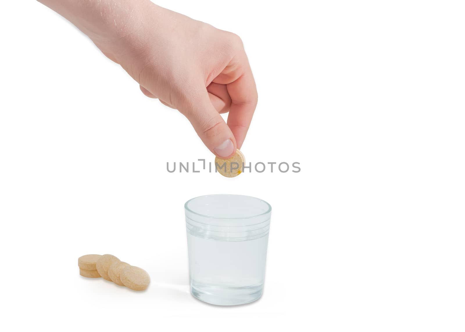 Effervescent medicinal tablet in the human hand above a glass of water and several same tablets beside on a light background
