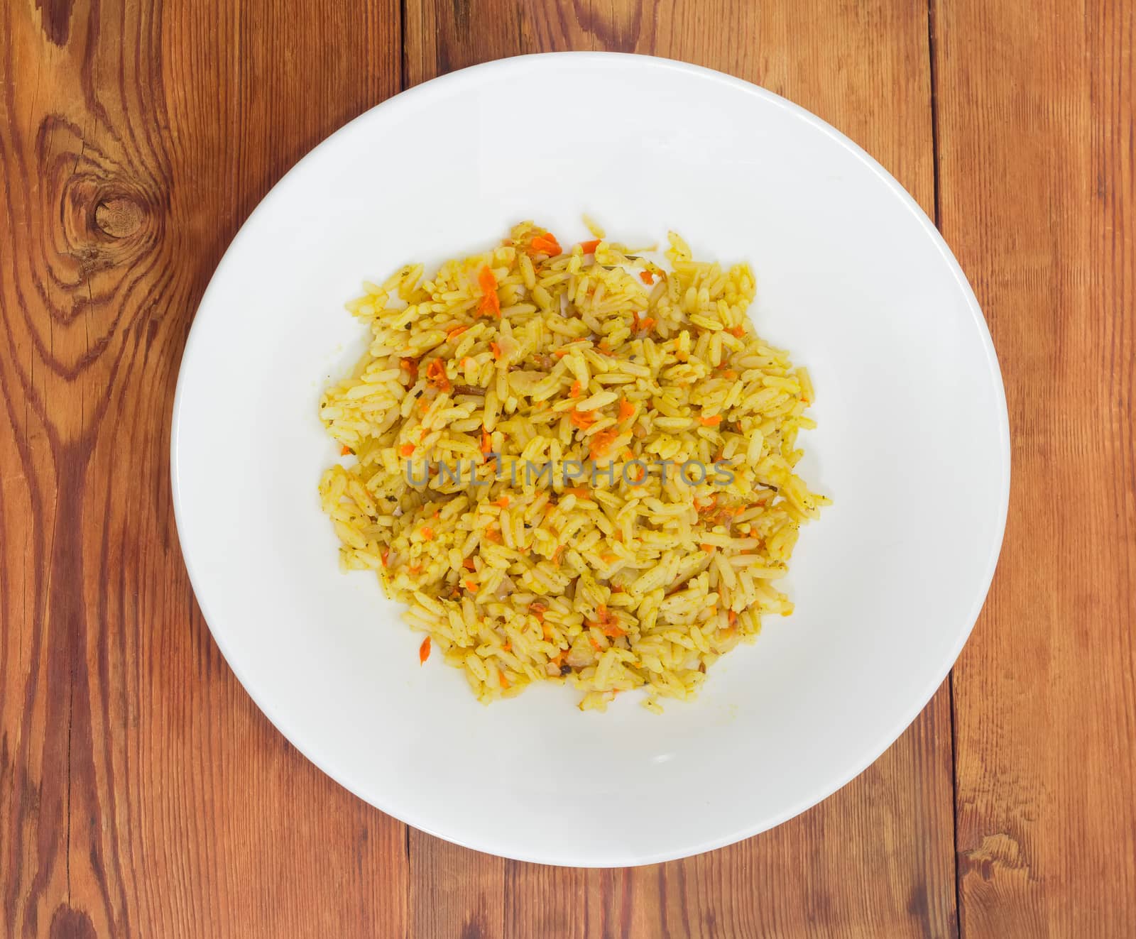 Top view of the white dish with rice cooked with carrots and spices on the surface of the old wooden planks
