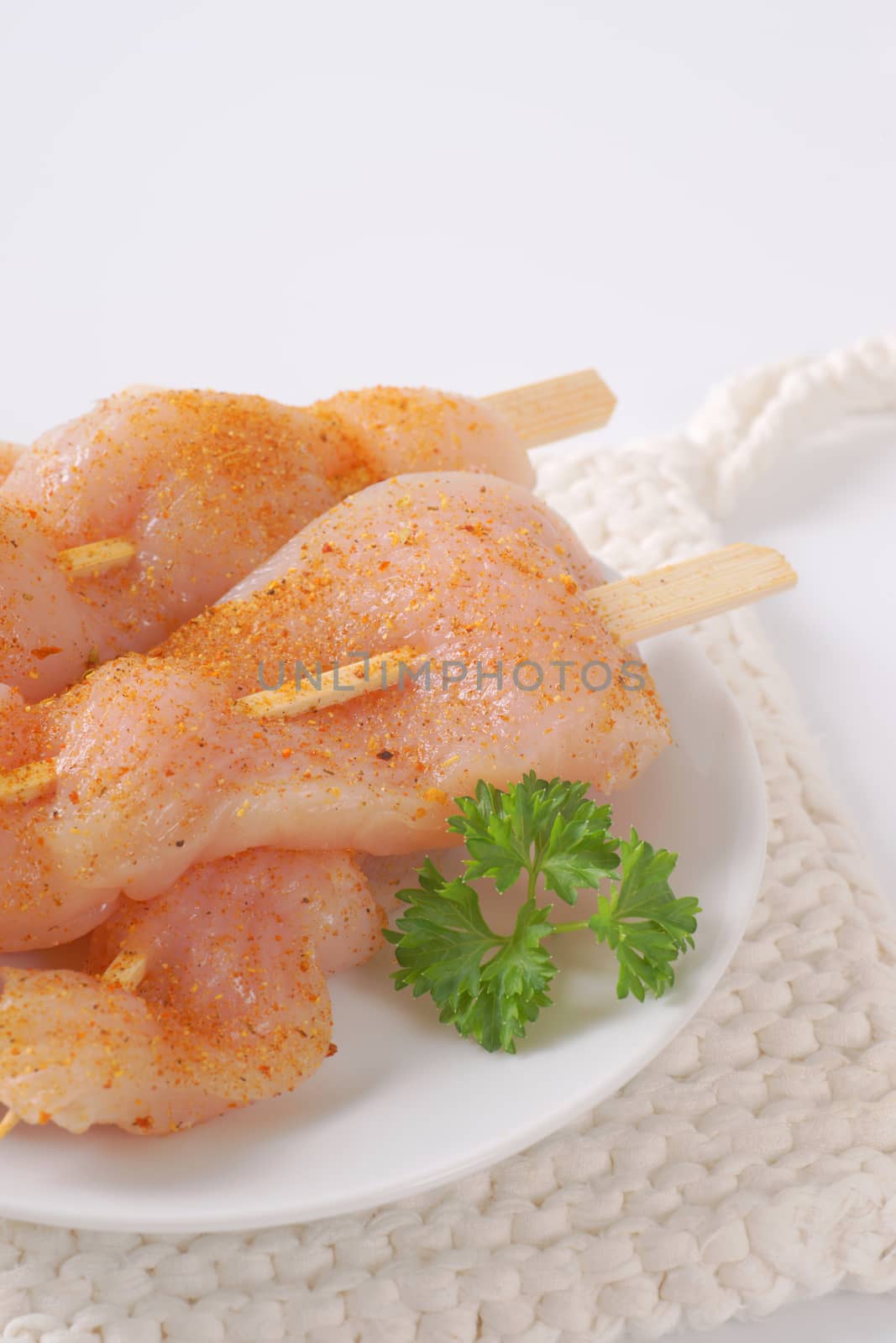 raw spiced chicken skewers on white plate