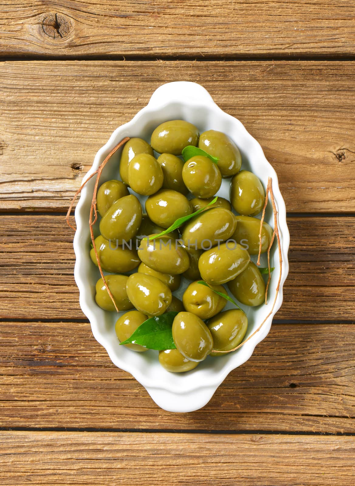 bowl of green olives on wooden background