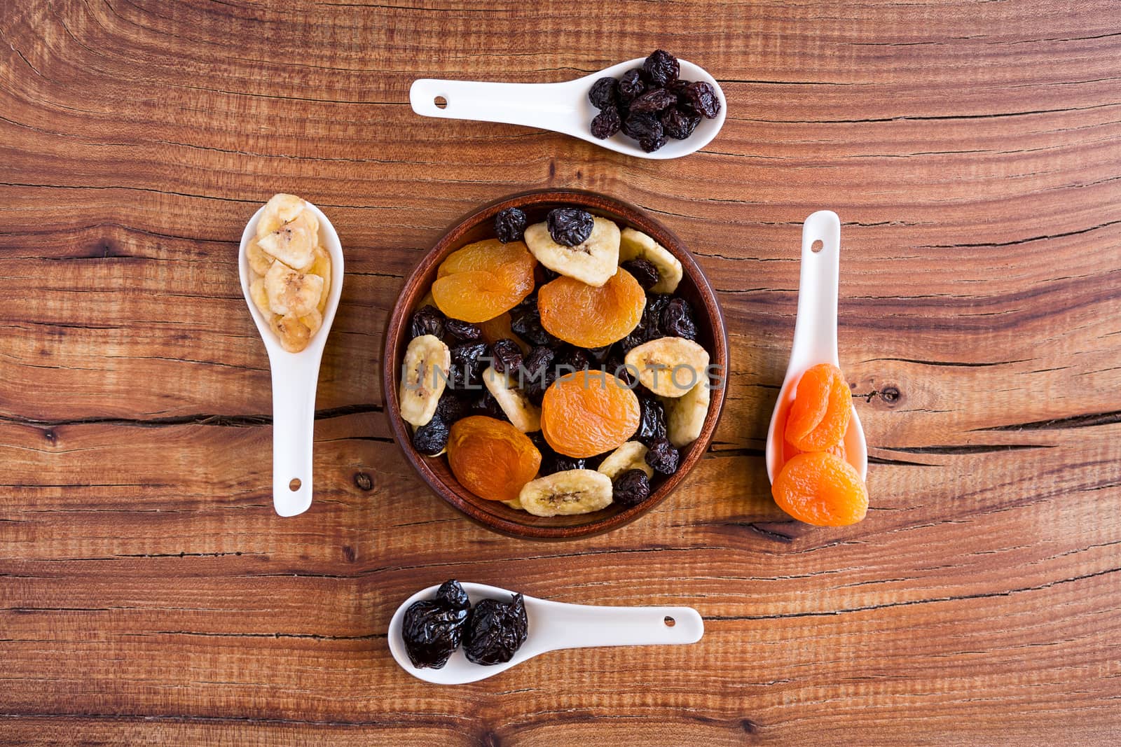 Mix of dried fruits in a wooden bowl over a rustic table seen from above
