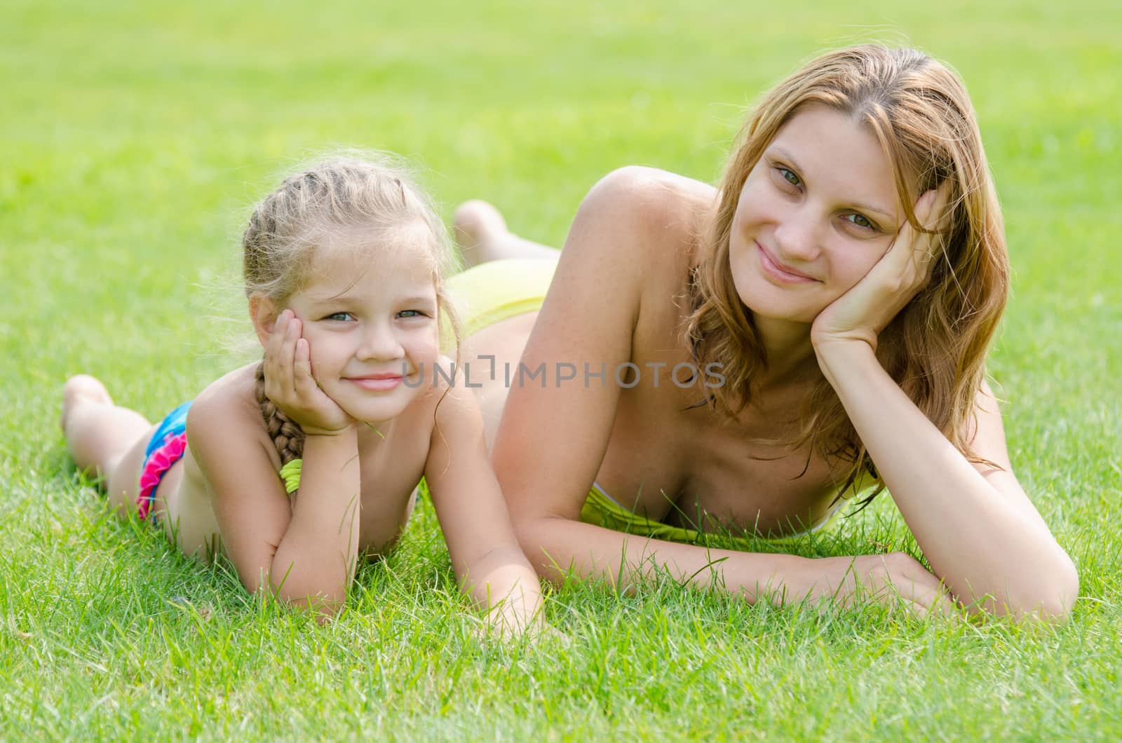 Young mother and five year old daughter lying on green grass and looking to the frame