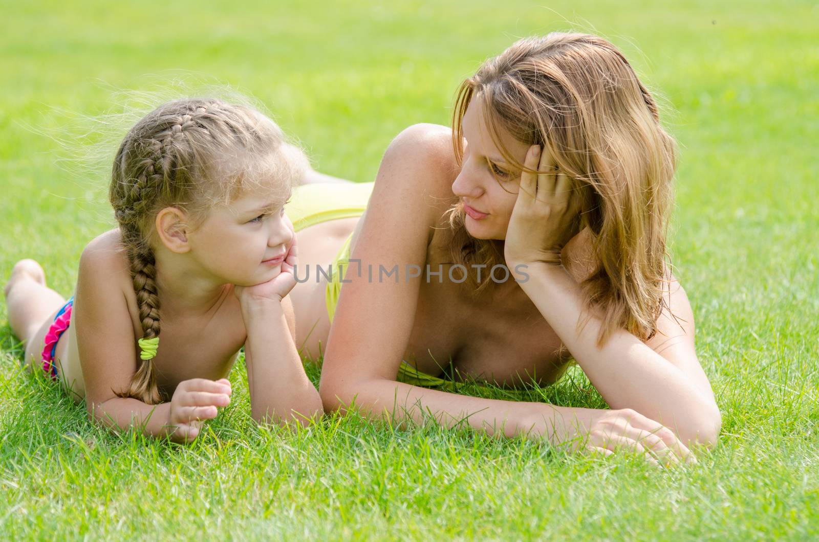 Young mother and five year old daughter lying on green grass and looking at each other by Madhourse