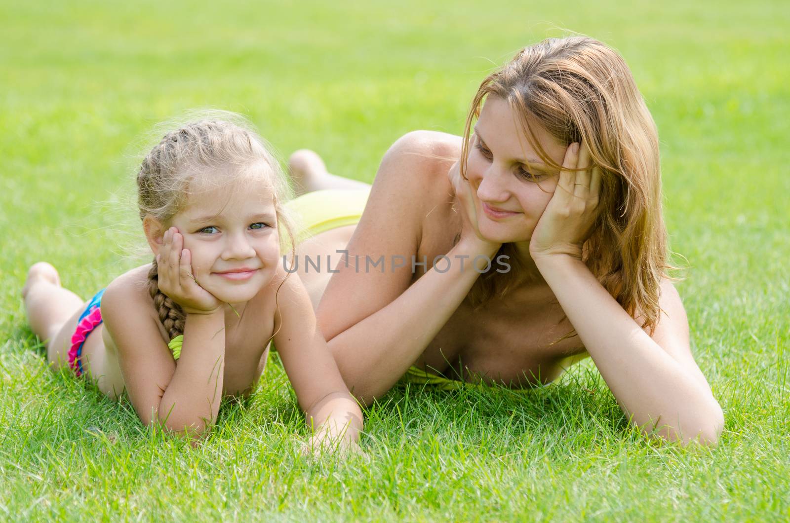 Young mother lying on green grass and looking at his five-year daughter who is lying near