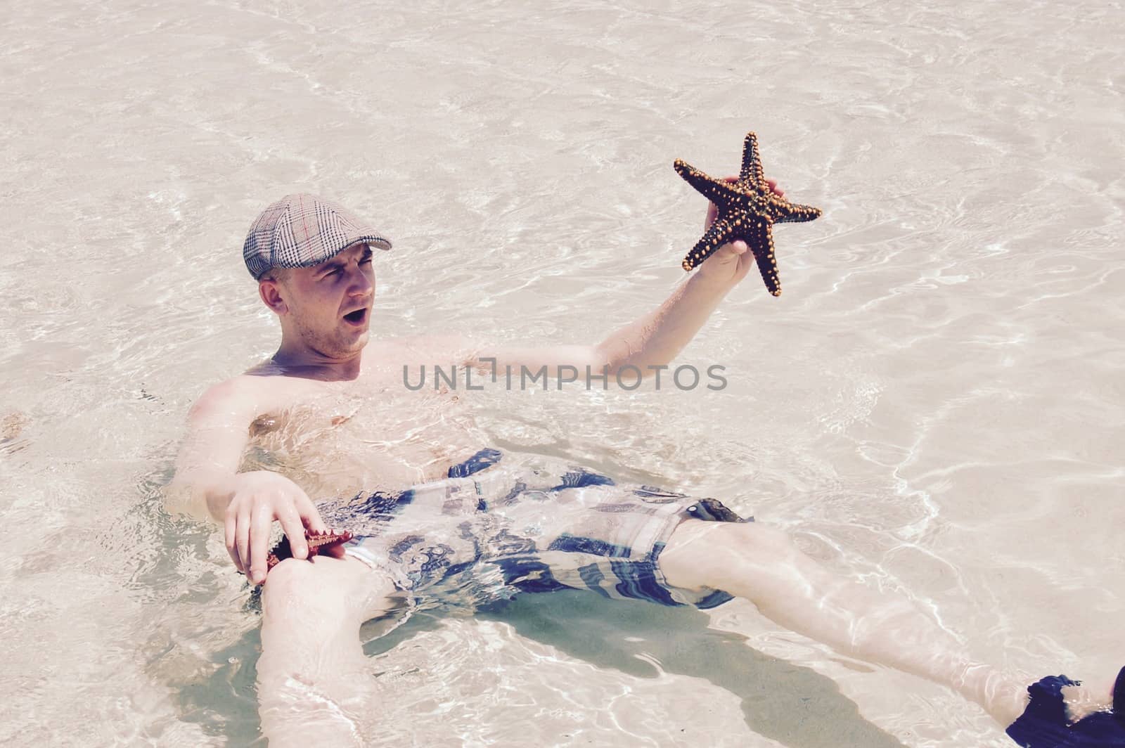 Young white man in water with a big starfish in his hand.