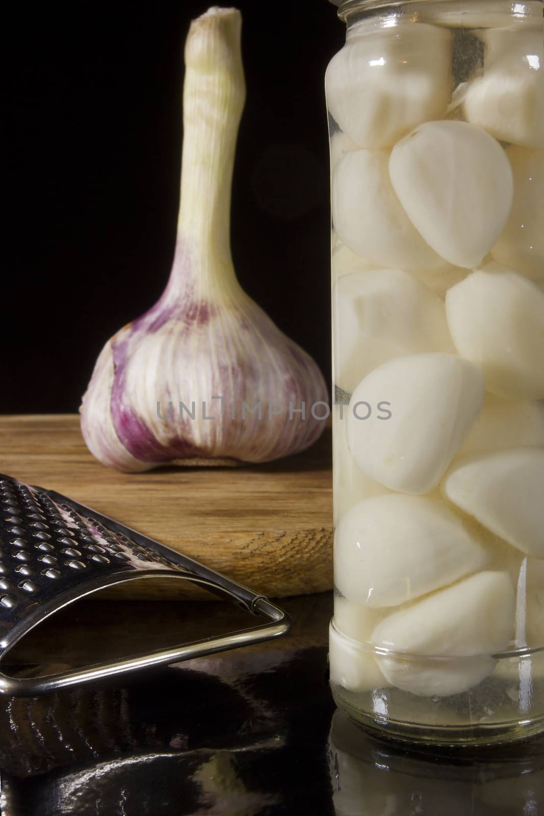 Marinated and fresh garlic with a grater on a dark background