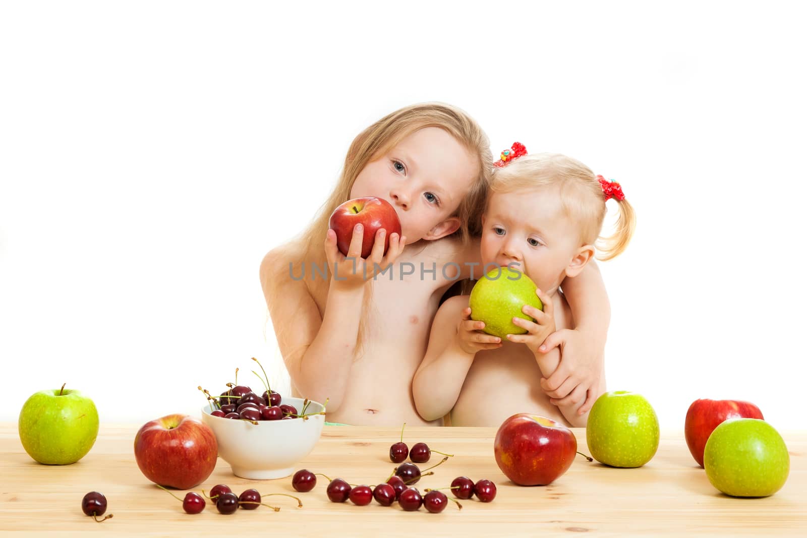 two little girls eat fruit at a table on the isolated background