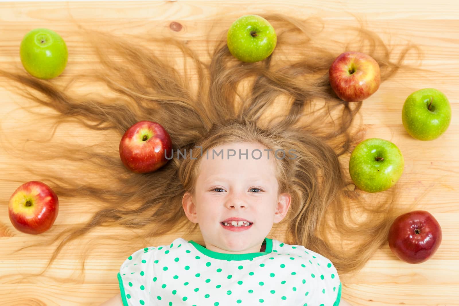 the little girl among apples on a wooden background