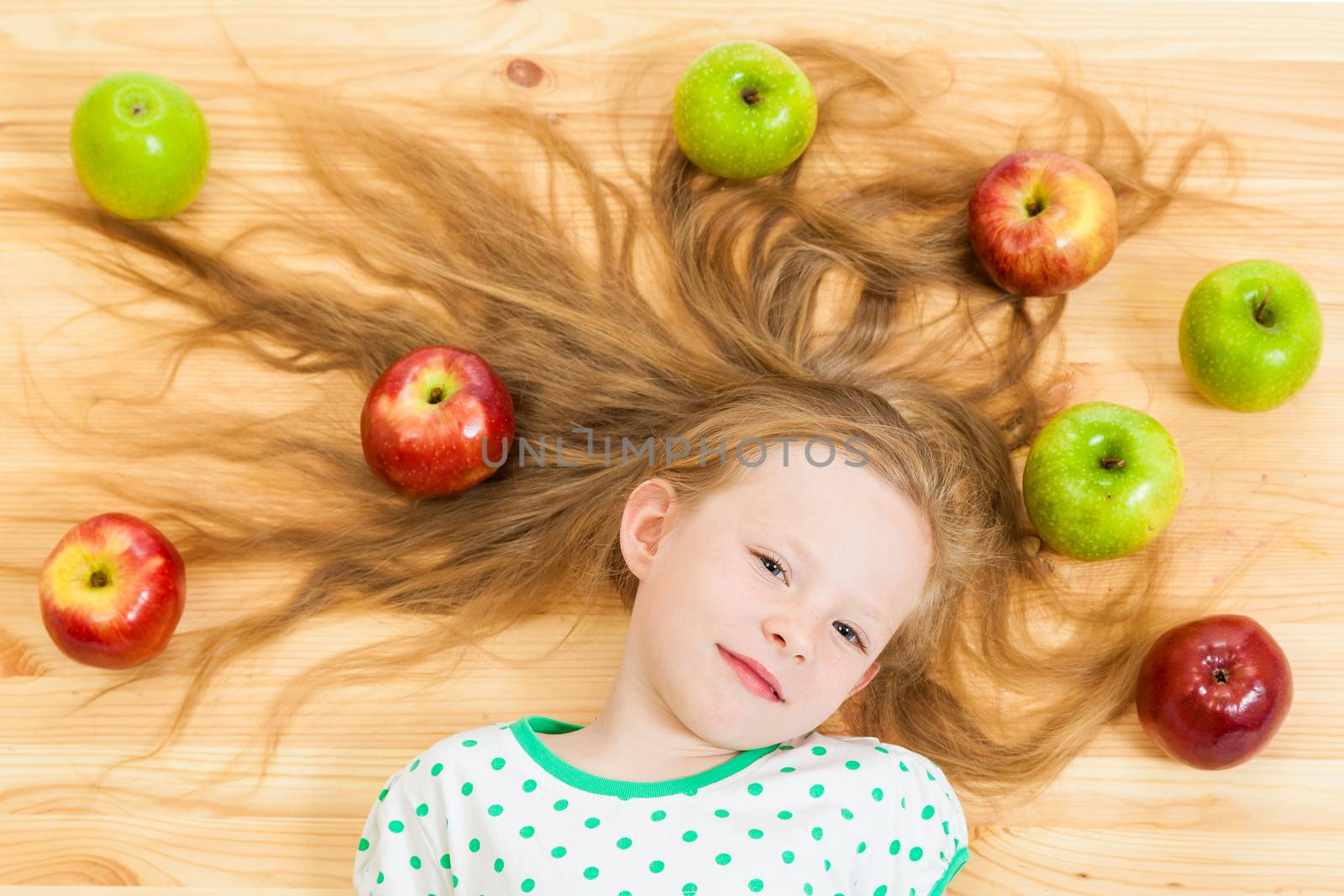 the little girl among apples on a wooden background