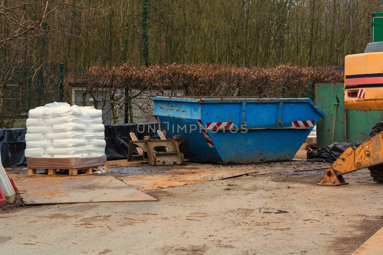 Blue container an excavator and pallet with white bags on a construction site in the forest.