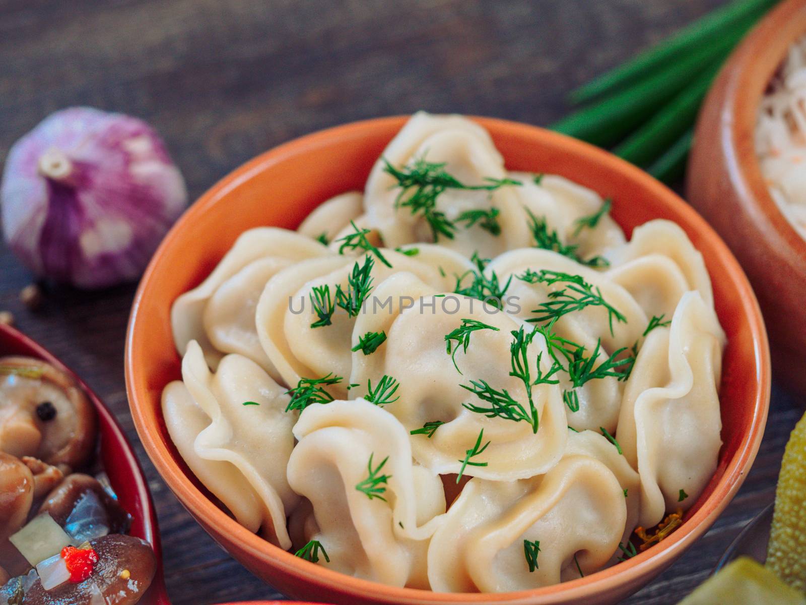 Closeup view of traditional russian food - pelmeni, ravioli or meat dumplings - on brown wooden table. Served with marinated mushrooms, sauerkraut, salted cucumbers, green onion and garlic. Copy space