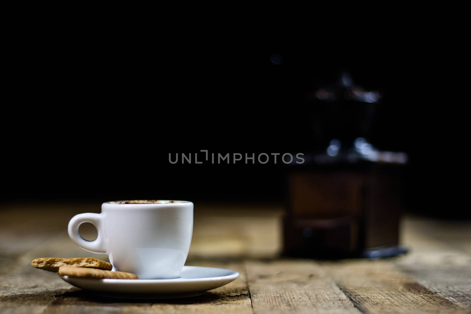 Freshly brewed coffee in mugs on a wooden table with a mill on a black background