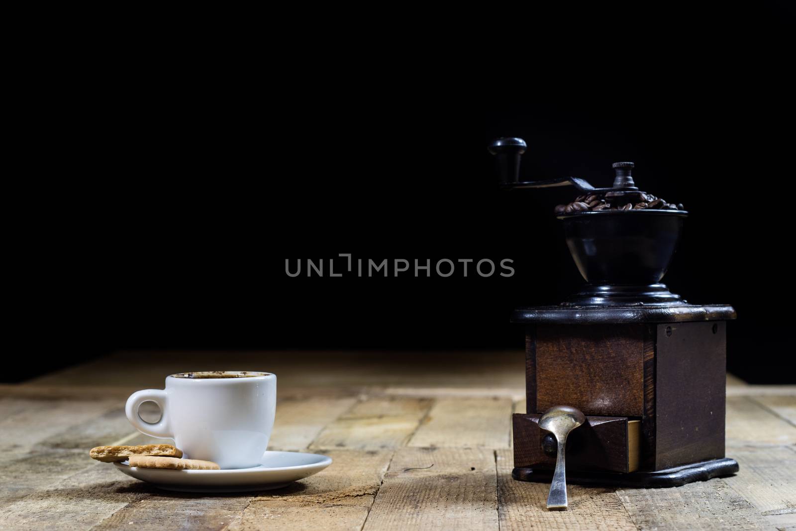 Freshly brewed coffee in mugs on a wooden table with a mill on a black background