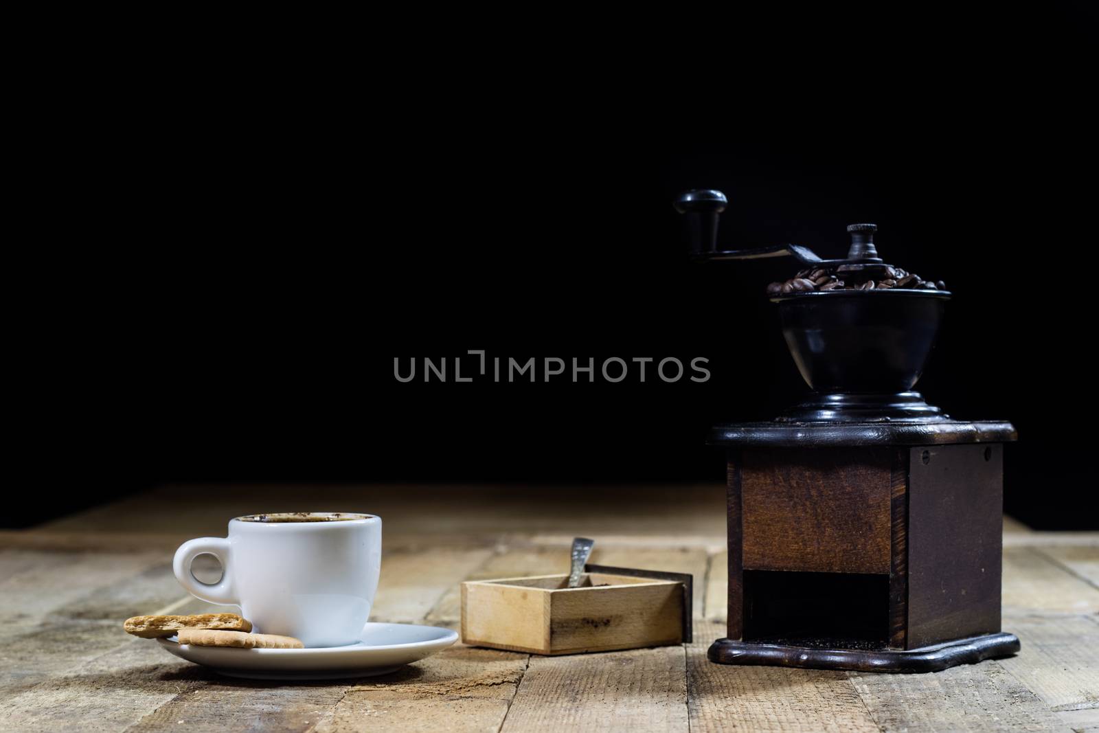 Freshly brewed coffee in mugs on a wooden table with a mill on a black background