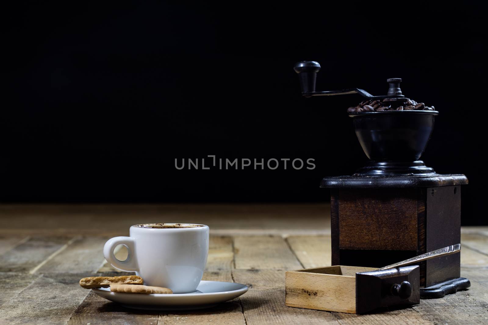 Freshly brewed coffee in mugs on a wooden table with a mill on a black background