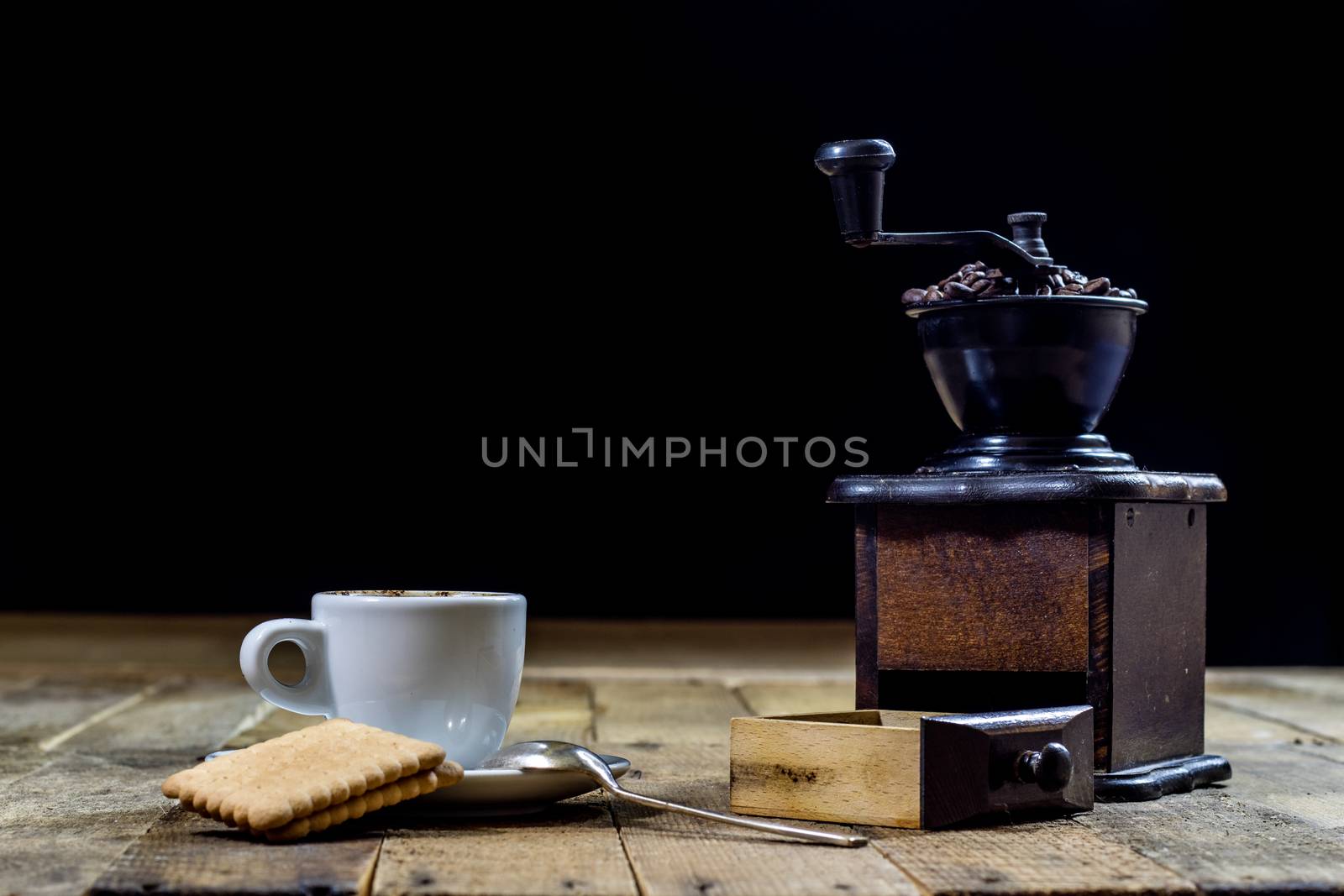 Freshly brewed coffee in mugs on a wooden table with a mill on a black background