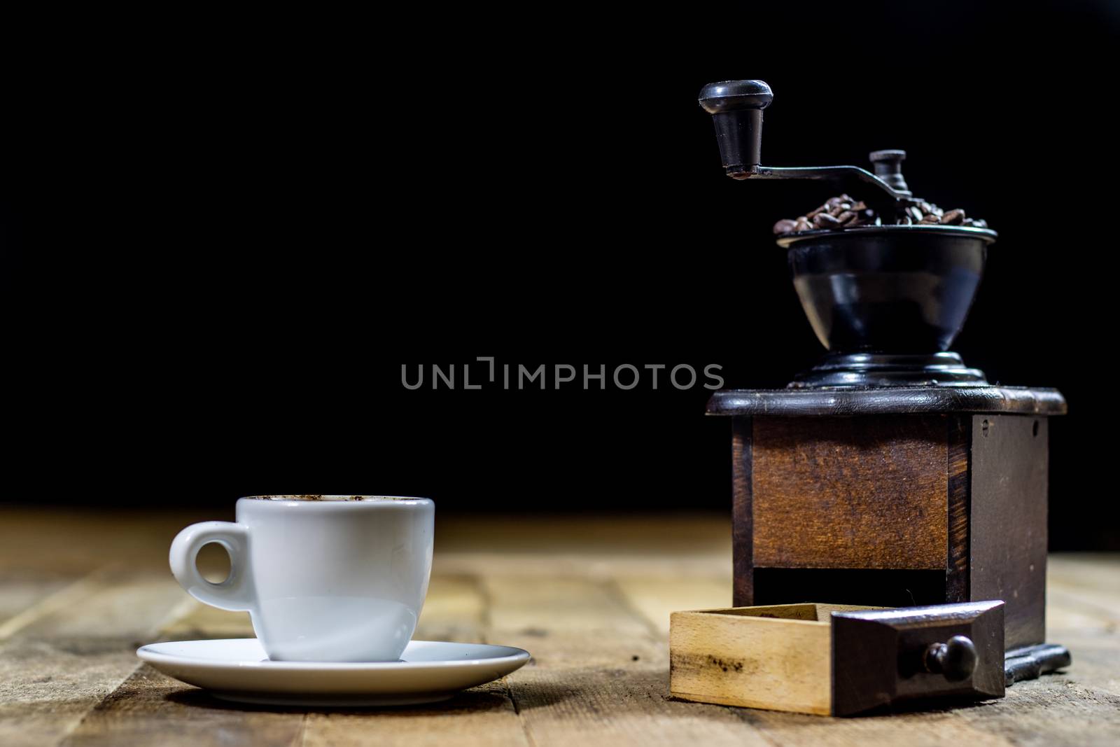 Freshly brewed coffee in mugs on a wooden table with a mill on a black background