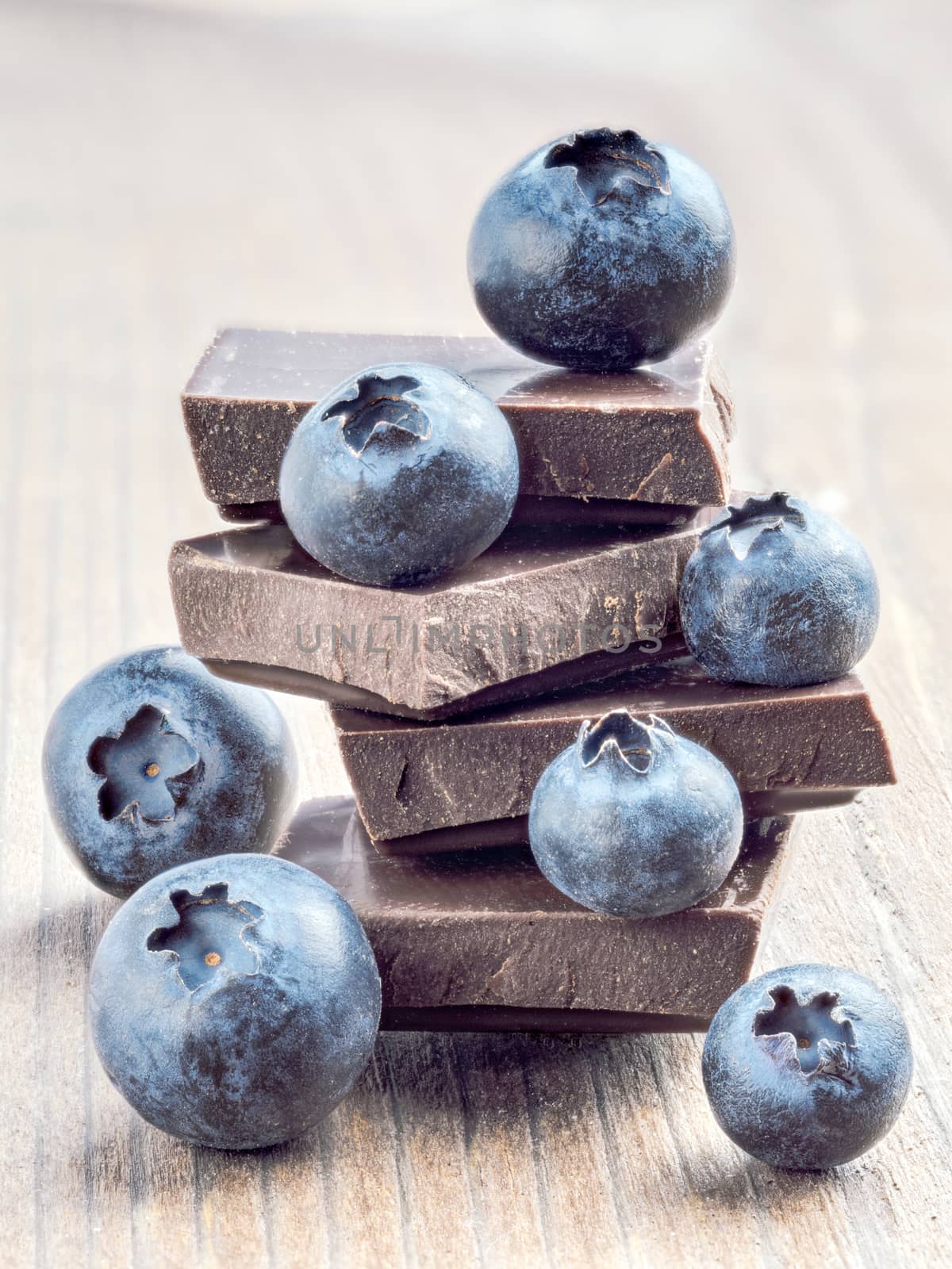 Stack of dark chocolate and fresh ripe blueberries. Blueberry and chocolate on wooden background. Vertical.