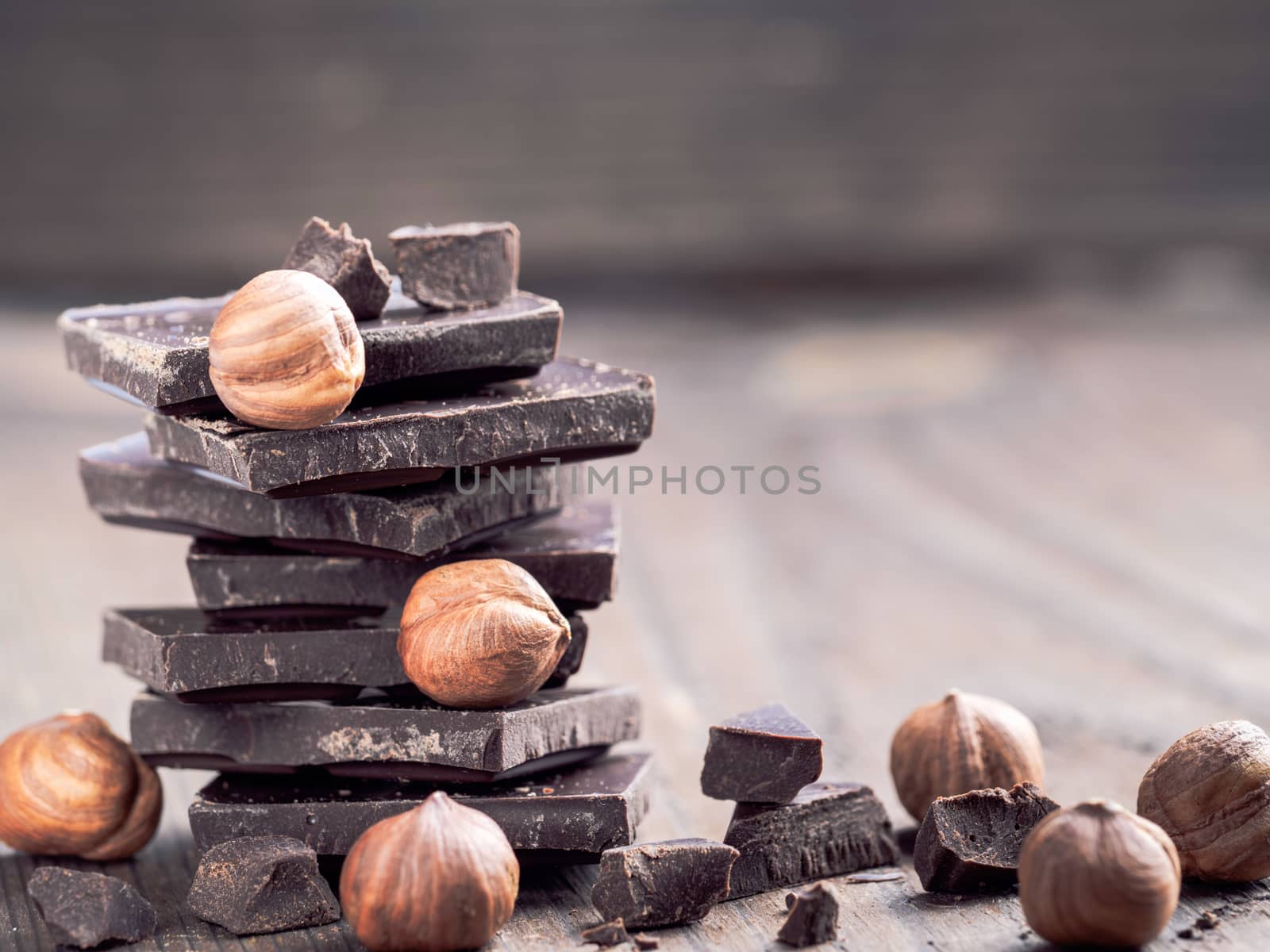 Stack of dark chocolate and whole hazelnut with copy space. Chocolate with crumbs and hazelnuts on wooden background.