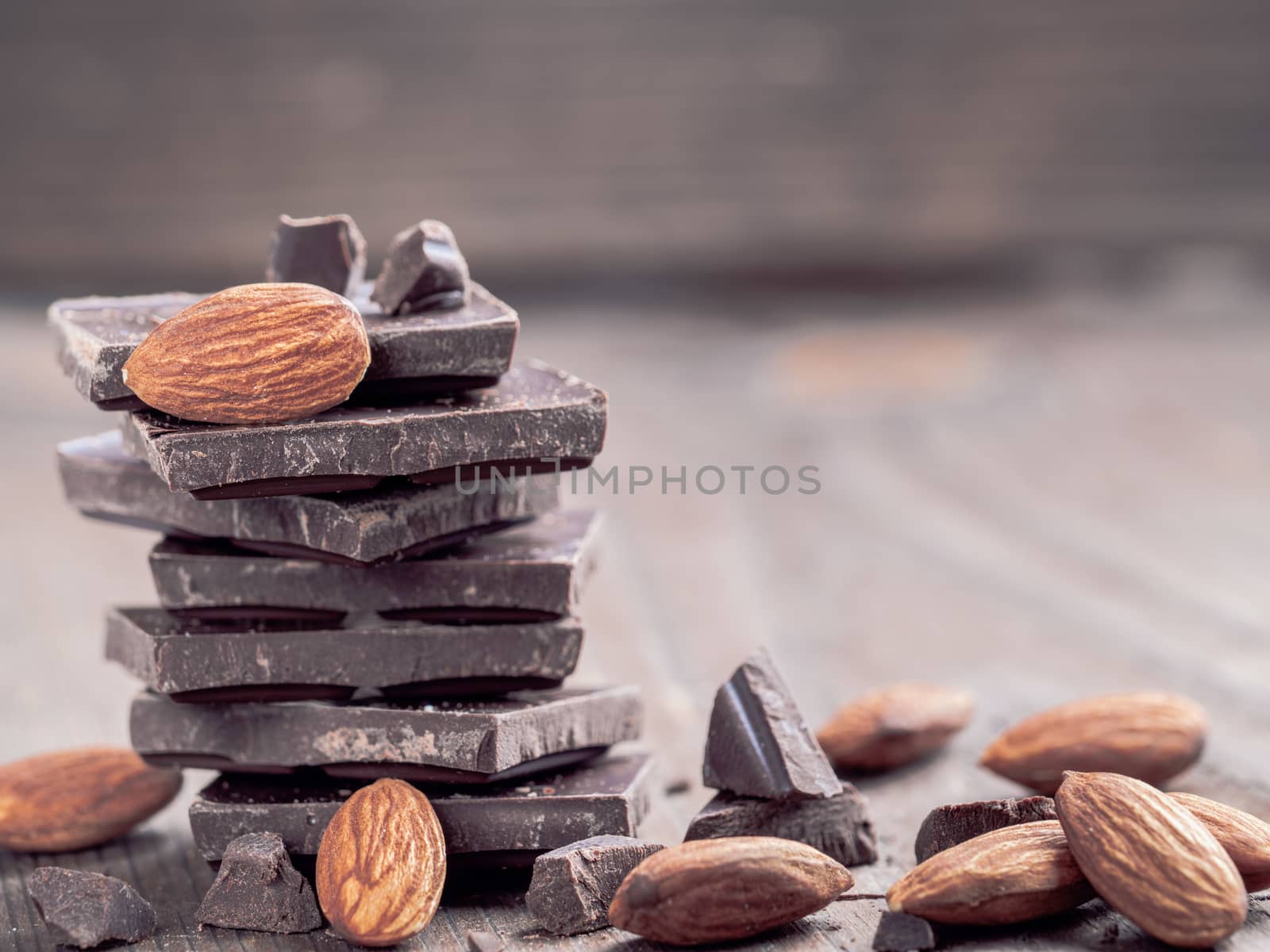 Stack of dark chocolate and whole almond with copy space. Chocolate with crumbs and almonds on wooden background.