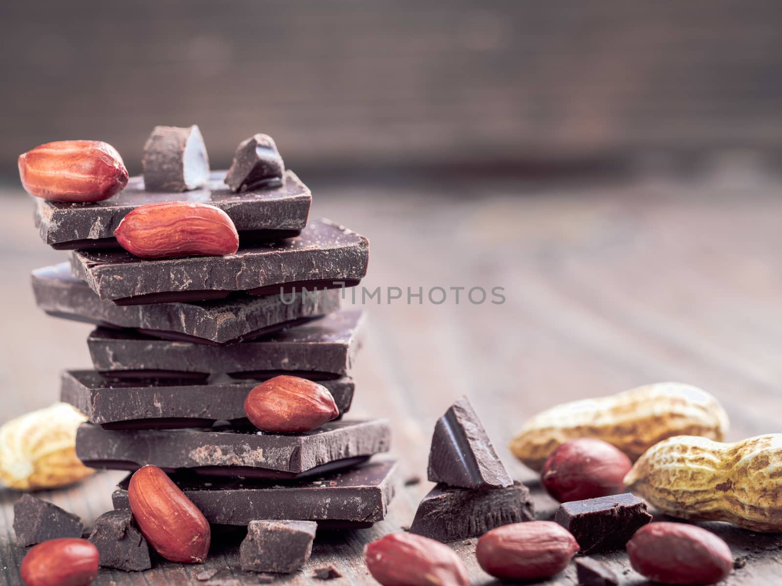 Stack of dark chocolate and peanut with copy space. Chocolate with crumbs and peanuts on wooden background.