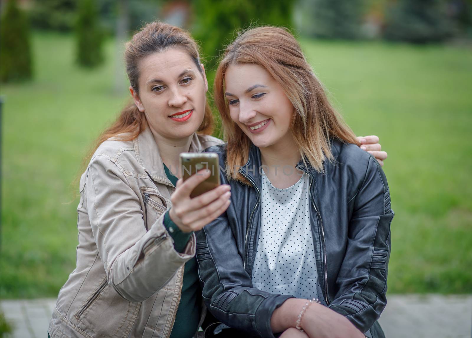 Two women friends sharing social media in smart phone outdoors by Angel_a