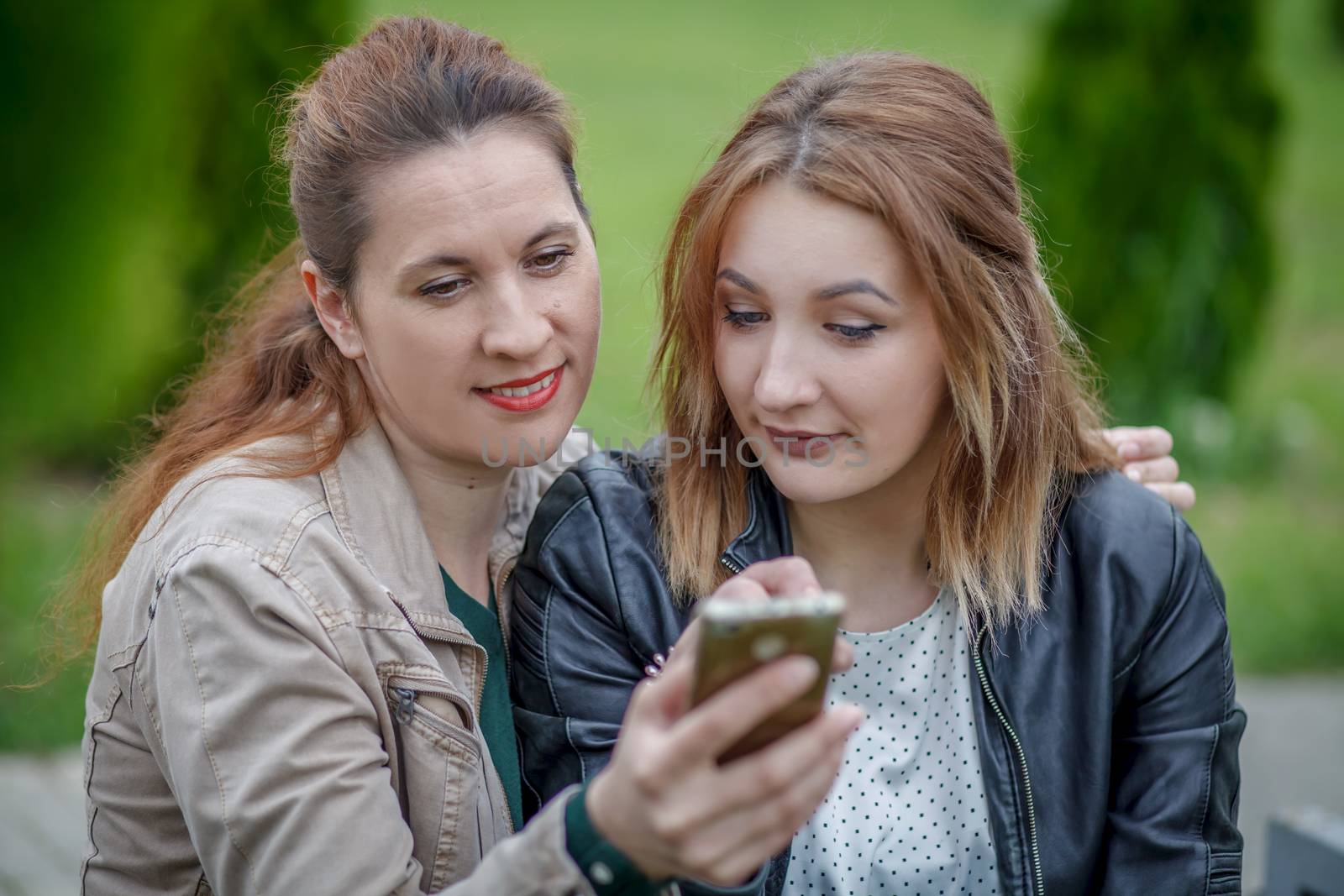Two women friends sharing social media in smart phone outdoors by Angel_a